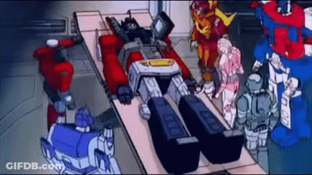 Transformers Standing Around Robot Laying On Bed GIF