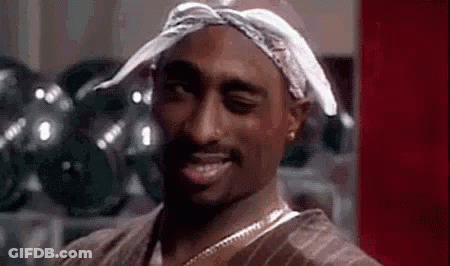 Tupac Shakur Is Wearing A Bandana On His Head And Smiling . GIF