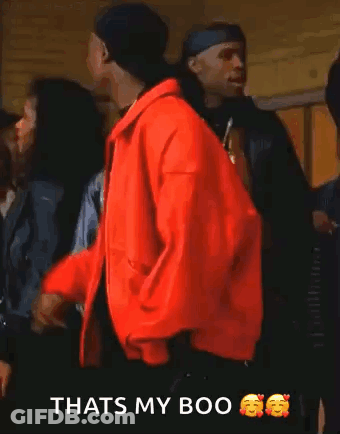 Tupac Shakur Is Wearing A Red Jacket And Smoking A Cigarette While Standing In Front Of A Group Of People . GIF