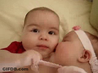 Two Babies Are Kissing Each Other On The Cheeks . GIF