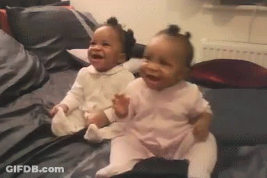 Two Babies Are Sitting Next To Each Other On A Bed Laughing . GIF