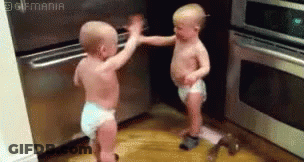 Two Babies In Diapers Are Standing Next To Each Other In A Kitchen And Giving Each Other A High Five . GIF