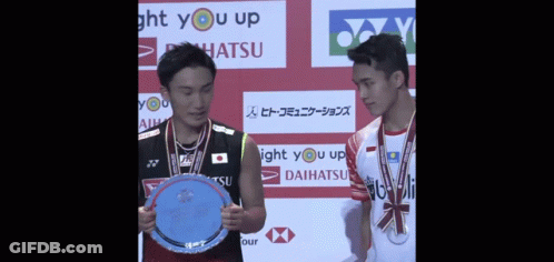Two Badminton Players Holding A Trophy In Front Of A Sign That Says Light You Up GIF