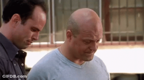 Two Bald Men Standing, One Looking Down GIF
