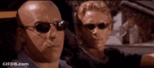 Two Bald Men Wearing Sunglasses Are Looking At Something GIF