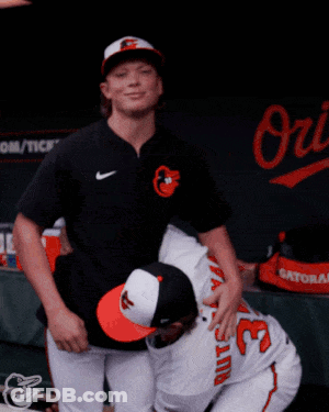 Two Baseball Players Are Hugging Each Other In Front Of A Sign That Says Orioles GIF