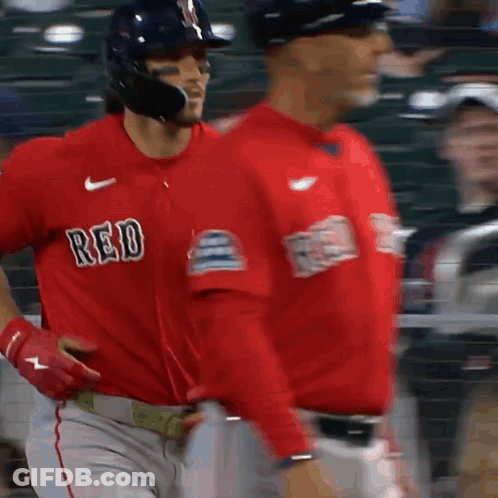 Two Baseball Players Wearing Red Jerseys Are Walking On A Field GIF