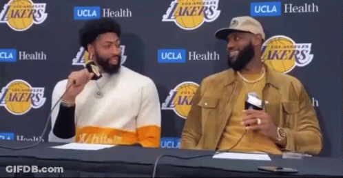 Two Basketball Players Are Sitting At A Table With A Lakers Logo In The Background GIF