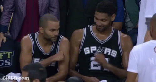 Two Basketball Players Are Sitting In The Stands Talking To Each Other During A Game . GIF