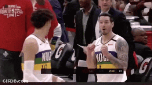 Two Basketball Players Are Talking To Each Other On The Court While A Man In A Suit Stands Behind Them . GIF