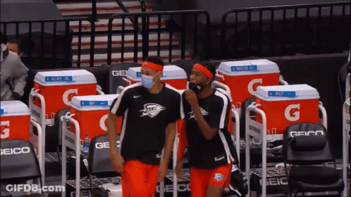 Two Basketball Players Wearing Face Masks Are Standing In Front Of A Row Of Gatorade Coolers GIF