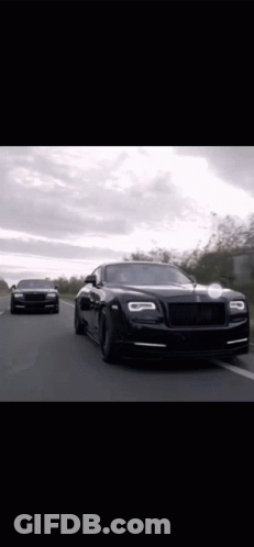 Two Black Rolls Royce Cars Are Driving Down A Road . GIF