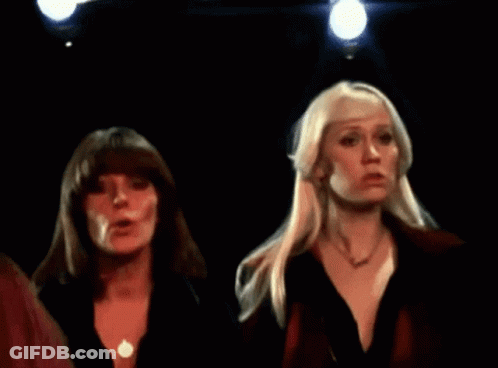 Two Blonde Women Are Standing In A Dark Room GIF