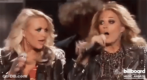 Two Blonde Women Are Standing Next To Each Other On A Stage Holding Microphones . GIF