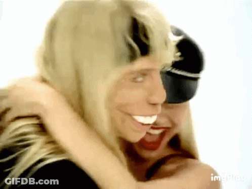 Two Blonde Women Hugging One In Black Hat GIF