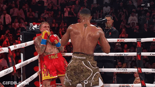 Two Boxers Are Fighting In A Boxing Ring While A Cameraman Takes A Picture . GIF