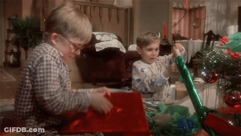 Two Boys In Pajamas Are Opening Christmas Presents In Front Of A Christmas Tree GIF