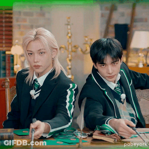 Two Boys In Suits And Ties Are Sitting At A Table With A Green Background That Says Pabeyork On It GIF
