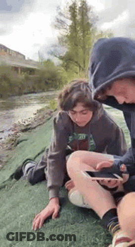 Two Boys Sitting By River Looking At Cell Phone GIF