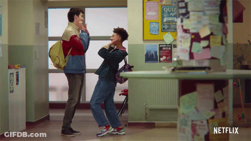 Two Boys Standing In Hallway Next To Quiz Bulletin Board GIF
