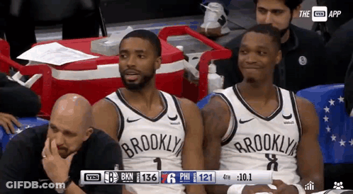 Two Brooklyn Nets Players Sit In The Stands During A Basketball Game GIF