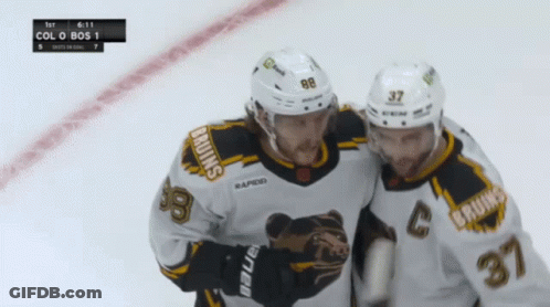 Two Bruins Hockey Players On The Ice With A Scoreboard In The Background GIF