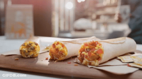 Two Burritos Are Sitting On A Wooden Cutting Board Next To A Smaller Burrito GIF