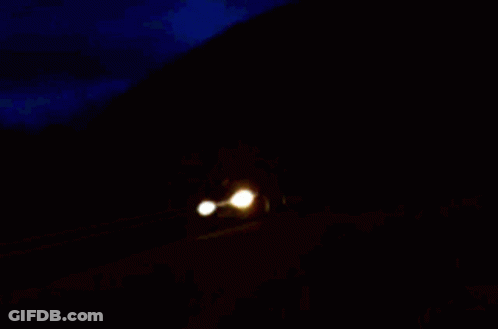 Two Cars Are Driving Down A Road At Night GIF