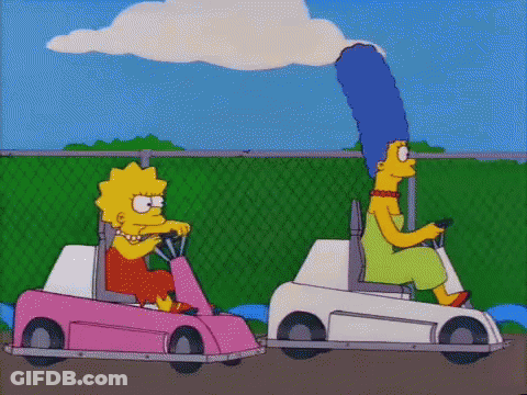 Two Cartoon Characters , Lisa Simpson And Marge Simpson , Are Driving Go Karts On A Track . GIF