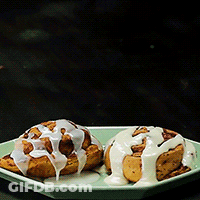 Two Cinnamon Rolls With White Frosting On A Plate GIF