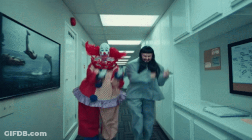 Two Clowns Are Walking Down A Hallway With A Lego Sign On The Wall Behind Them GIF