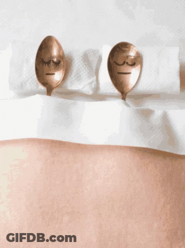 Two Copper Spoons With Faces Drawn On Them Are Laying On A Bed GIF