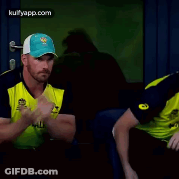 Two Cricket Players Are Sitting Next To Each Other In A Dark Room . GIF