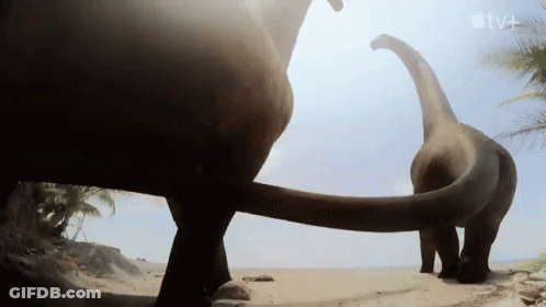 Two Dinosaurs Standing On Beach With TV+ Logo GIF