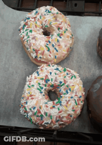 Two Donuts With Sprinkles On Them Are On A Table GIF