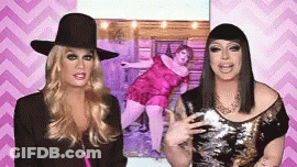 Two Drag Queens Are Standing Next To Each Other In Front Of A Picture Of A Fat Woman . GIF