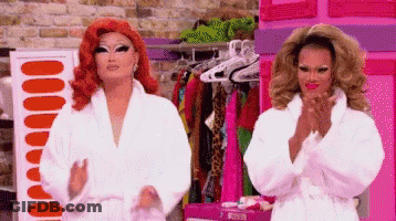 Two Drag Queens In White Robes Standing Together GIF