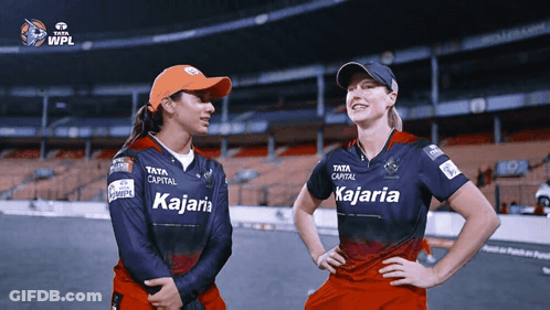 Two Female Cricket Players Wearing Kajaria Jerseys Stand Next To Each Other GIF