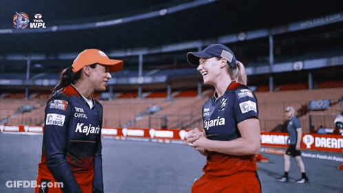 Two Female Cricket Players Wearing Kalari Jerseys Laugh Together GIF