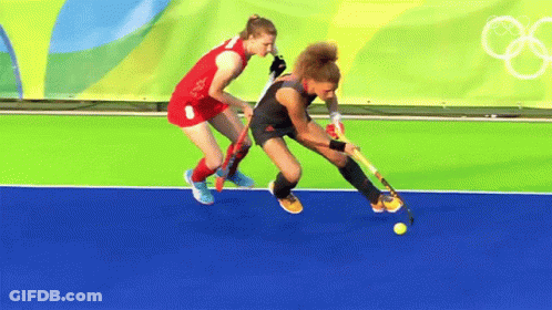 Two Female Field Hockey Players Are Playing On A Field GIF