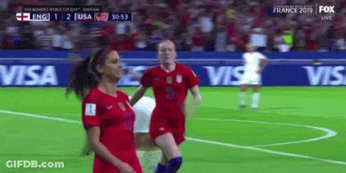 Two Female Soccer Players On A Field With Visa Advertisements Behind Them GIF