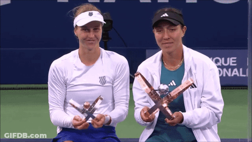 Two Female Tennis Players Holding Trophies In Front Of A Sign That Says Que GIF