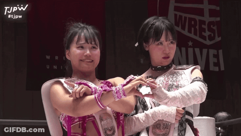Two Female Wrestlers Posing In Front Of Wrest Sign GIF
