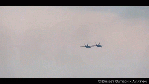 Two Fighter Jets Flying In A Cloudy Sky With Ernest Gutschik Aviation Written On The Bottom Right GIF