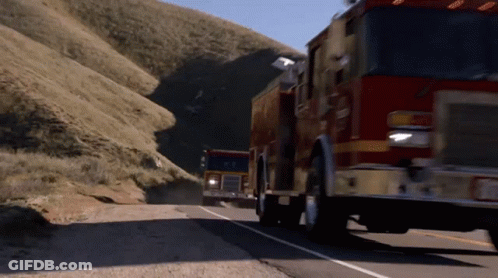 Two Fire Trucks Are Driving Down A Road With A Mountain In The Background GIF