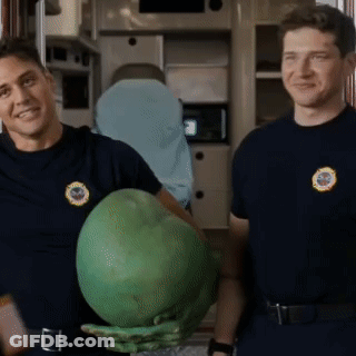 Two Firefighters Are Standing Next To Each Other Holding A Large Green Object GIF