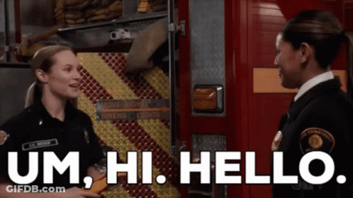 Two Firefighters Are Standing Next To Each Other In Front Of A Fire Truck And Talking To Each Other . GIF