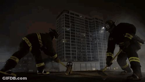 Two Firefighters In Front Of Building With Hammer And Chainsaw GIF