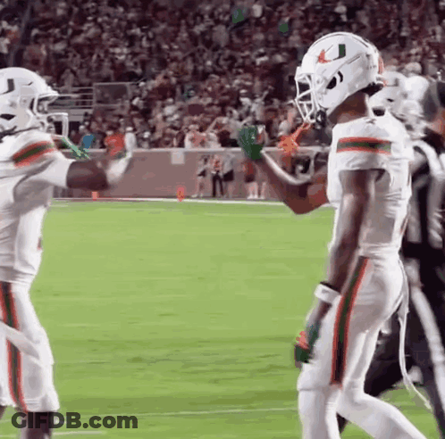 Two Football Players Are Giving Each Other High Fives On The Field . GIF