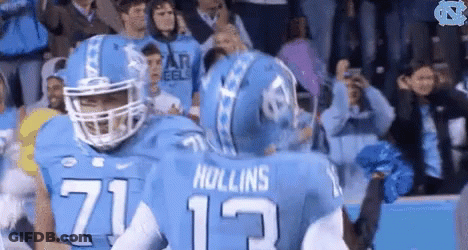 Two Football Players Hugging Each Other In Front Of A Crowd GIF